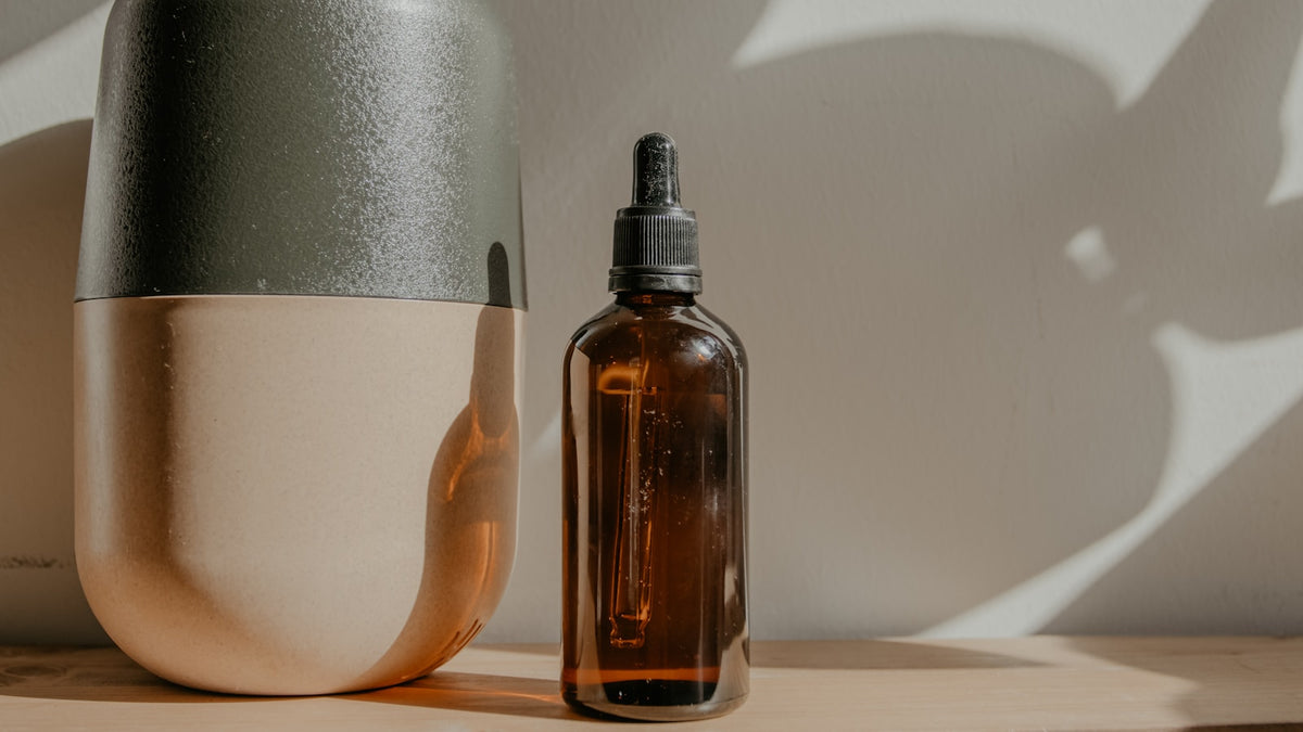 Flacon de sérum en verre ambré et vase en céramique, ombres feuillage